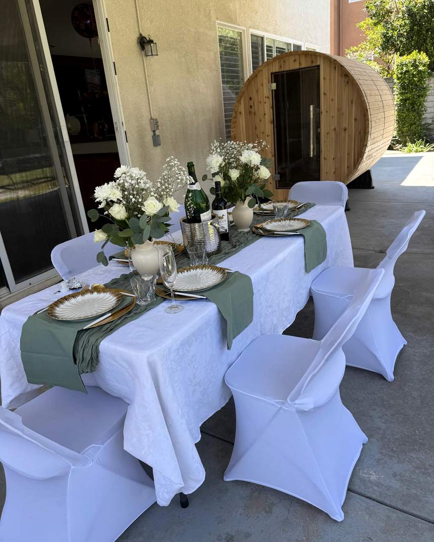 Outdoor table set with white linen, sage runner, gold chargers, and white florals